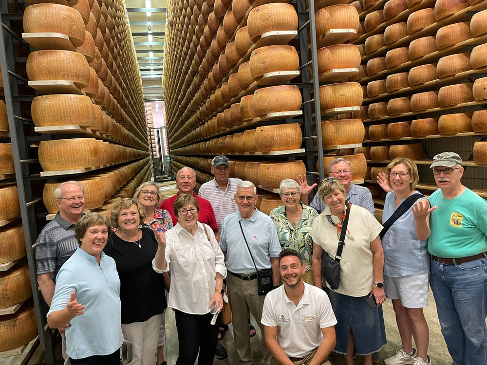 Tour group posing between towering shelves of cheese wheels