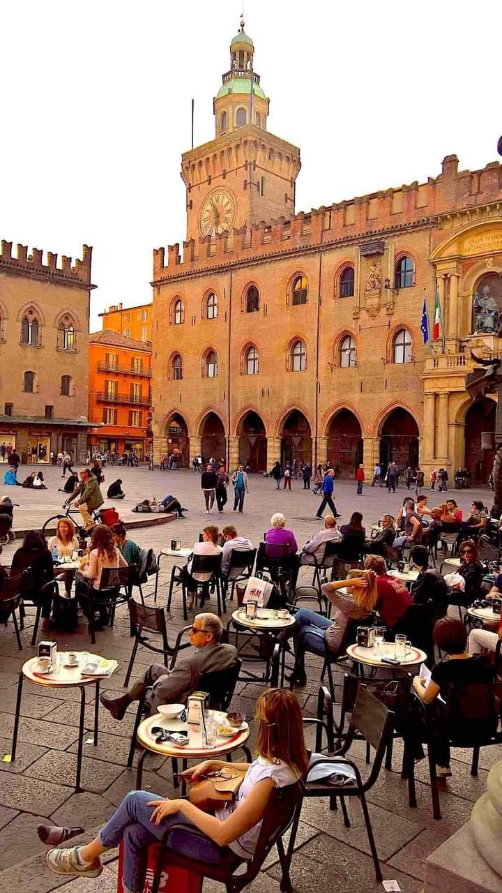 Busy café tables on a piazza below a medieval clock tower