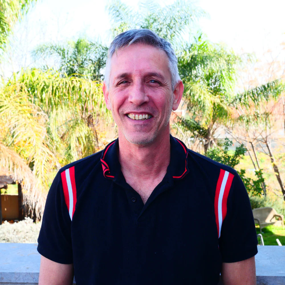 Smiling man in a black polo shirt in front of palm trees