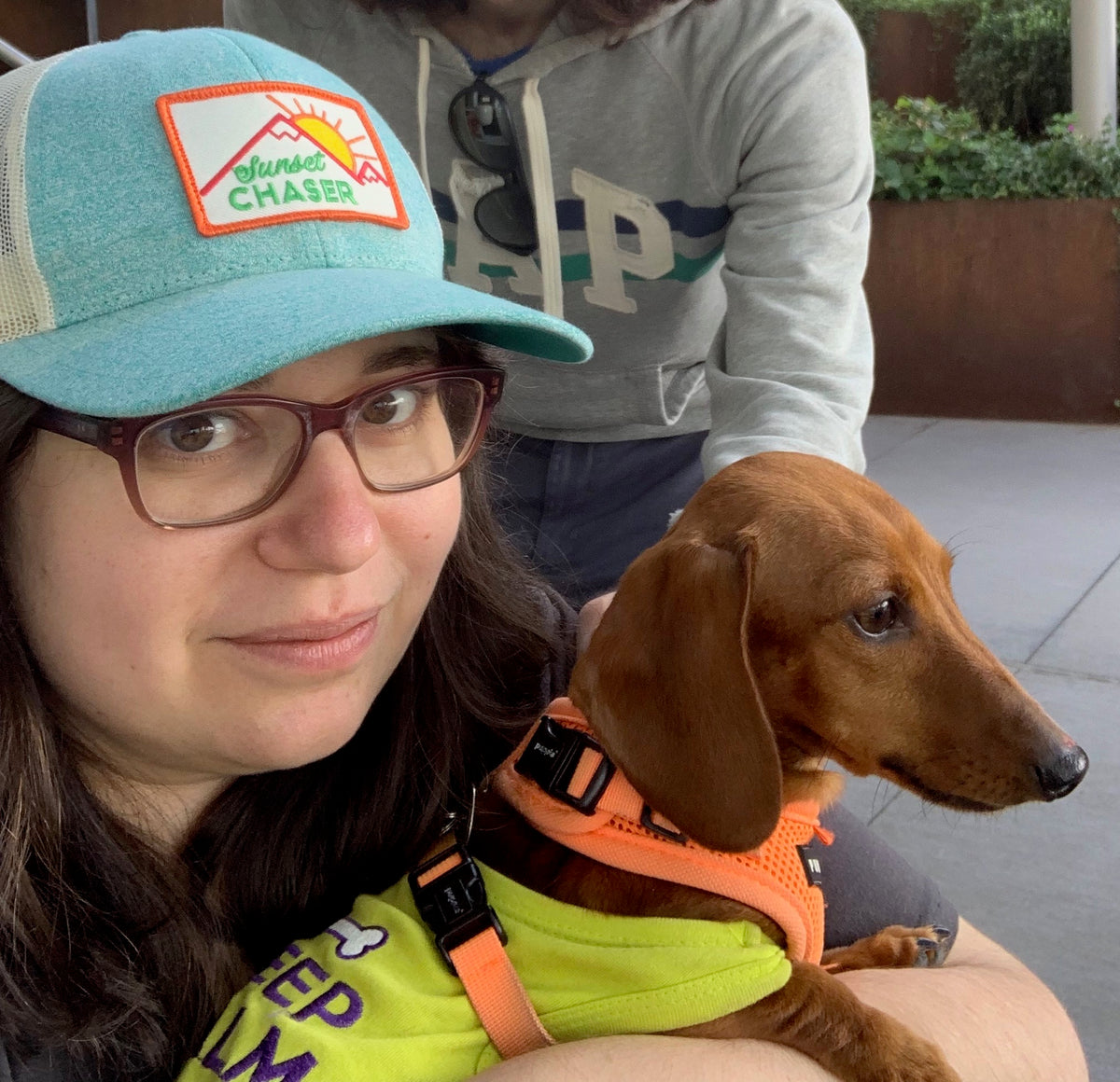Smiling woman in a cap and glasses holding a dachshund