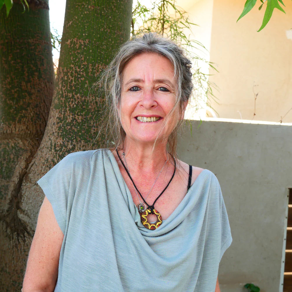 Smiling woman with grey hair in a light blue top standing by a tree