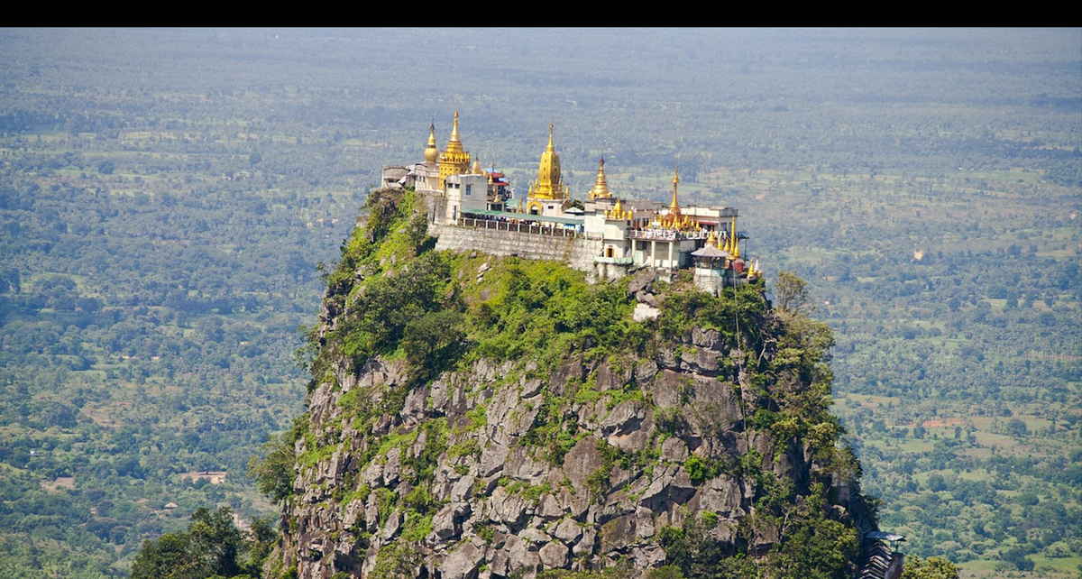Hilltop monastery with golden spires crowning a rocky outcrop over plains