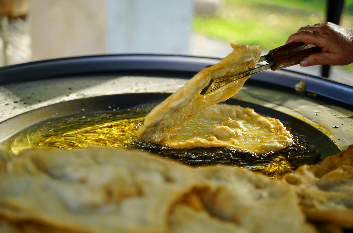 Flatbread frying in a large pan of oil being turned with tongs