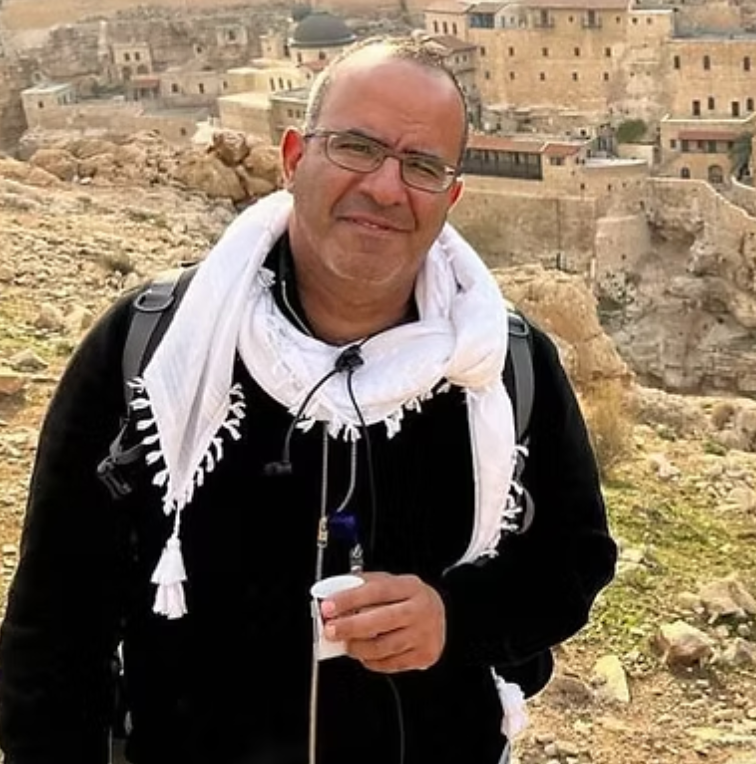 Smiling man in a white scarf with a stone hillside village behind
