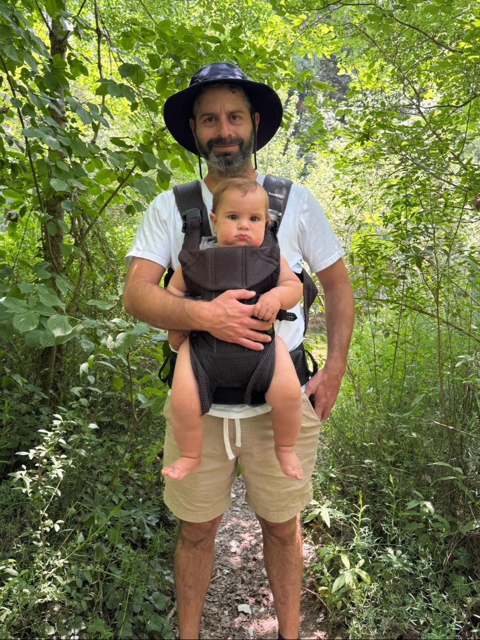 Man in a sun hat carrying a baby in a carrier on a forest trail