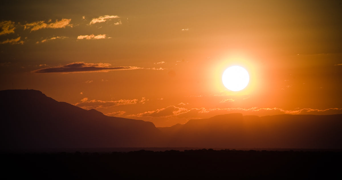 Orange sun setting over silhouetted hills on the savanna