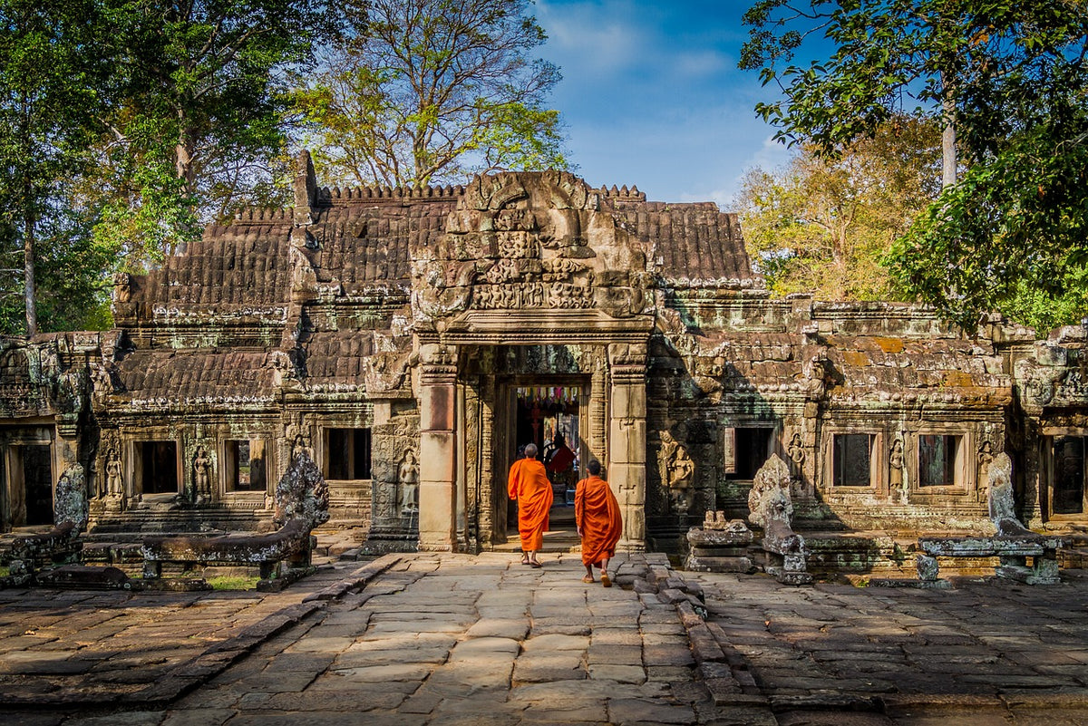 Two monks in orange robes walking into an ancient stone temple