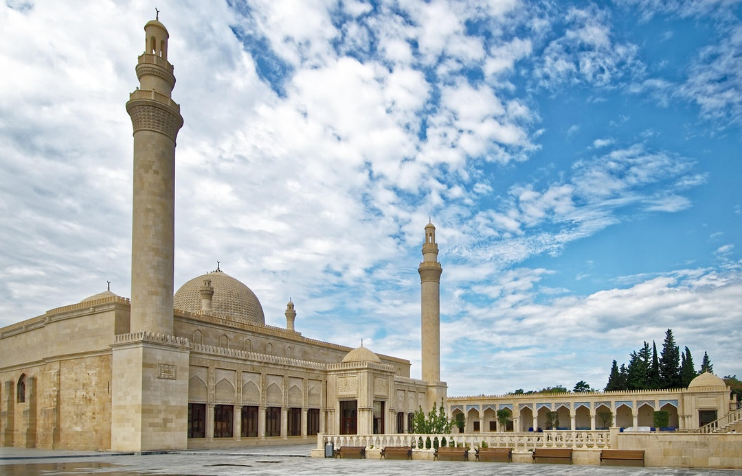 Pale stone mosque with tall minarets under a cloudy blue sky