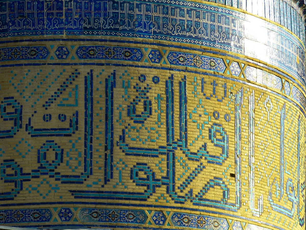 Golden mosaic tilework with blue calligraphy wrapping a curved dome drum
