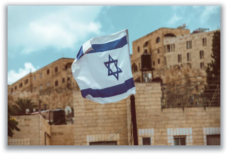 Israeli flag waving in front of old sandstone buildings under a blue sky