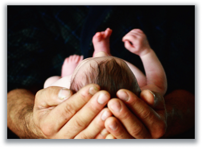 Adult hands cradling a newborn baby against a dark background