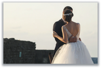 Bride and groom embracing beside an old stone wall at sunset