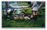 Family roasting food on sticks over a campfire on the grass