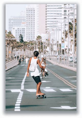 Skateboarder riding down a palm-lined city street between high-rise buildings