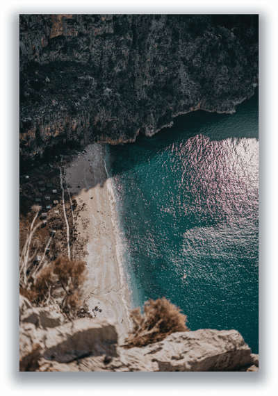Turquoise sea cove beneath rocky cliffs, seen from above