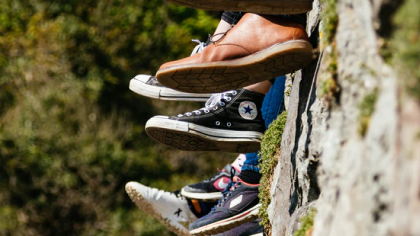Travellers' feet in sneakers dangling over a mossy rock ledge