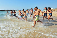 Group of young people running into the sea on a sunny beach