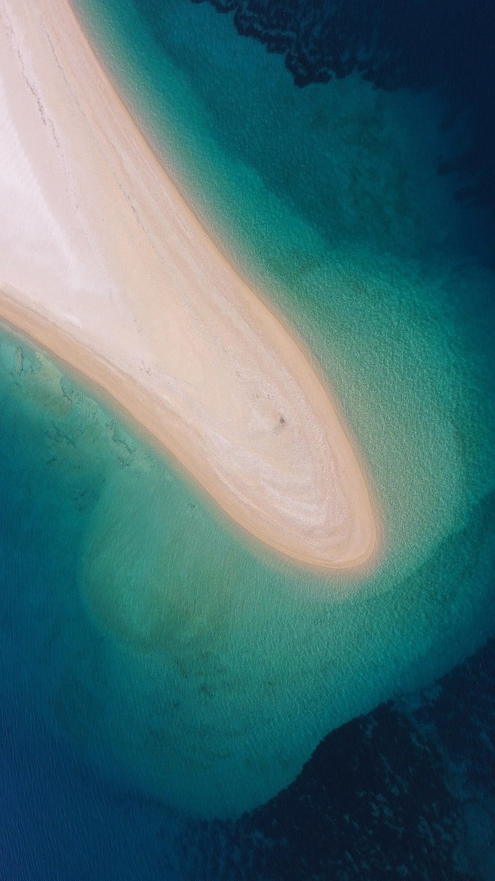 Aerial view of a curving white sandbar in turquoise and deep blue sea