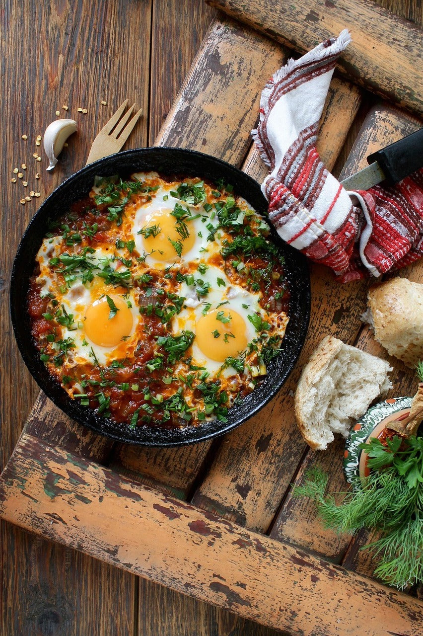 Eggs baked in tomato sauce in a cast-iron pan with bread and herbs
