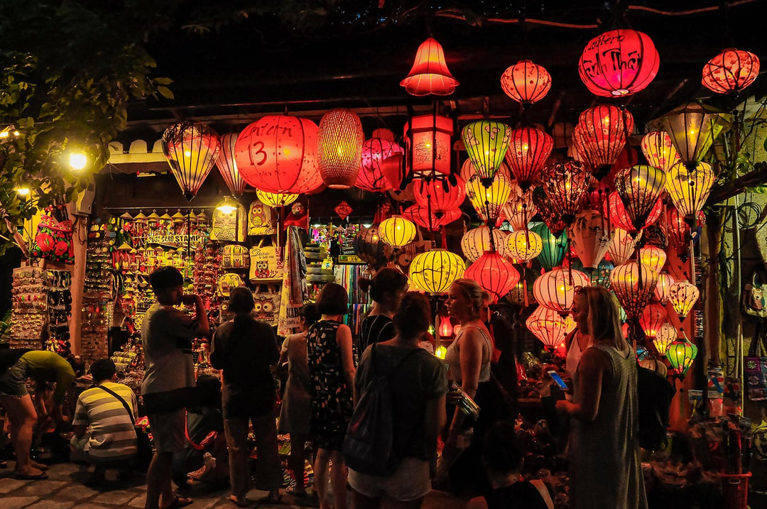 Crowd browsing a night market stall hung with glowing colourful silk lanterns