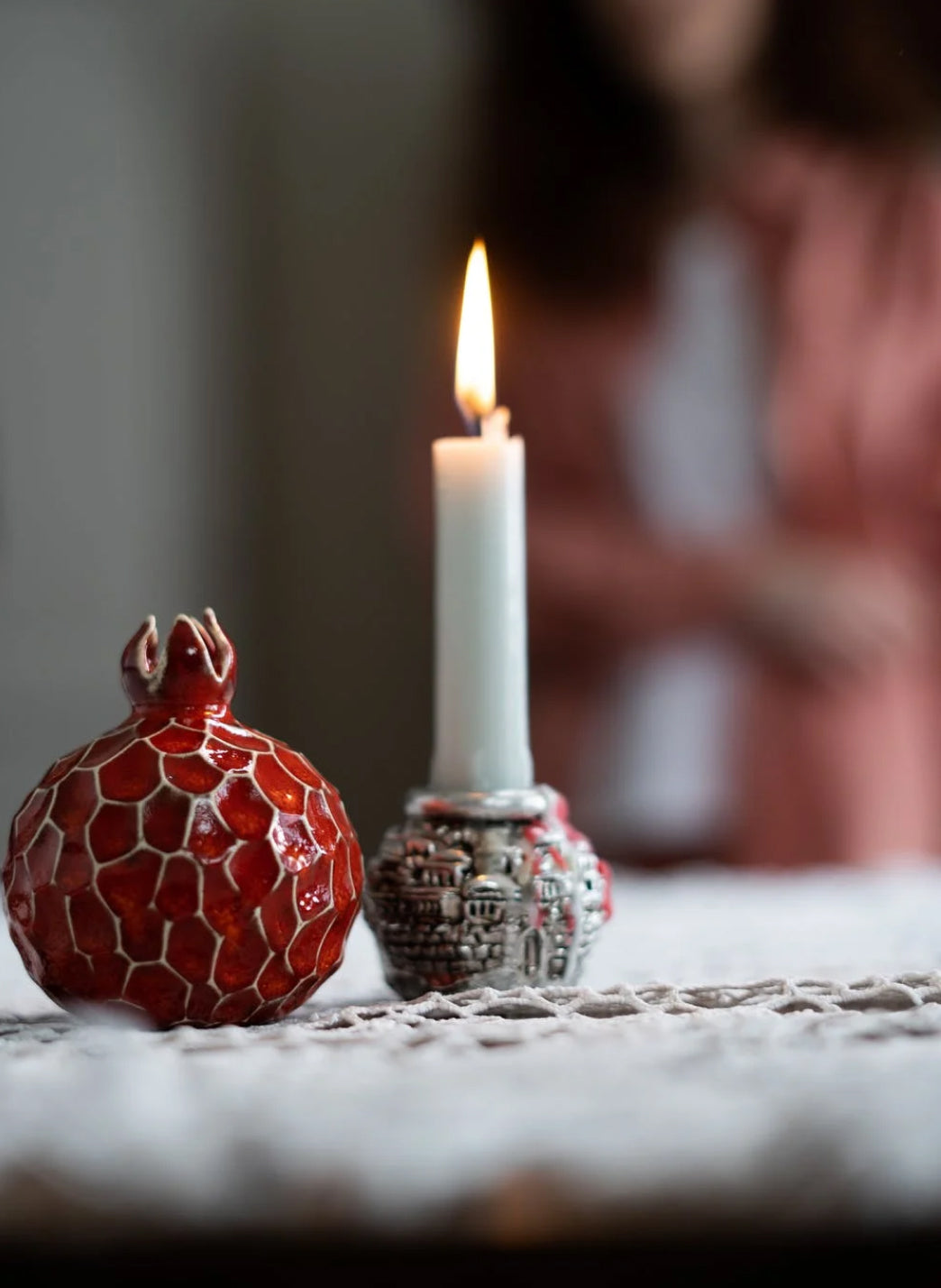 Shabbat candle beside a red ceramic pomegranate on a lace tablecloth