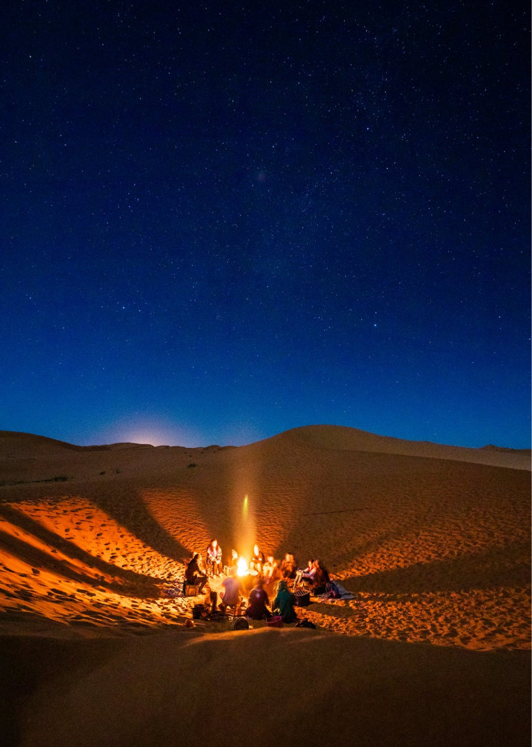 Group gathered around a campfire in the desert dunes under a starry sky