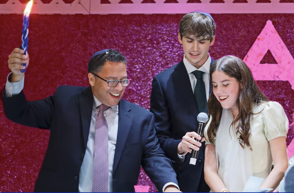 Man raising a lit braided candle beside a teen boy and girl at a celebration