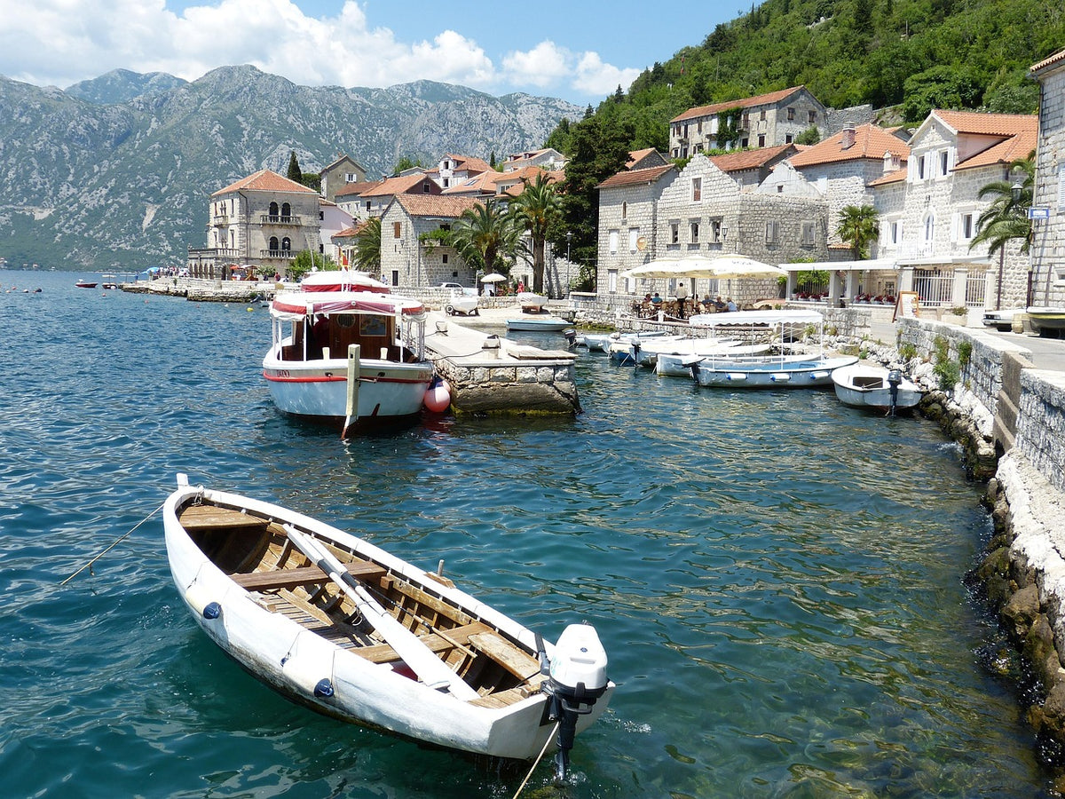 Small boats moored along a stone waterfront town below mountains