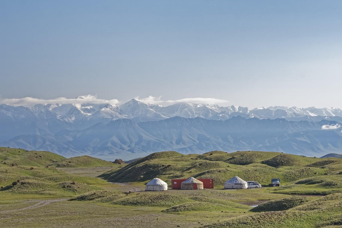 Yurts on green hills below a snow-capped mountain range