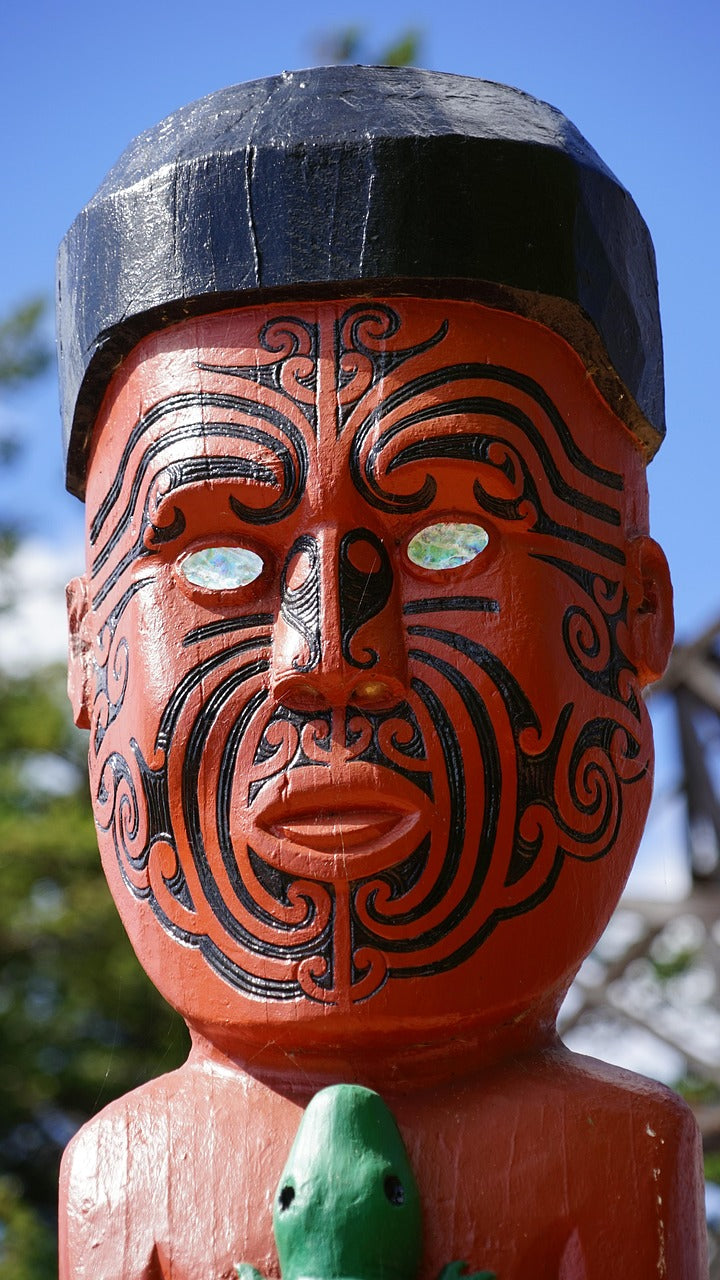 Carved wooden figure with red face and black spiral tattoo patterns