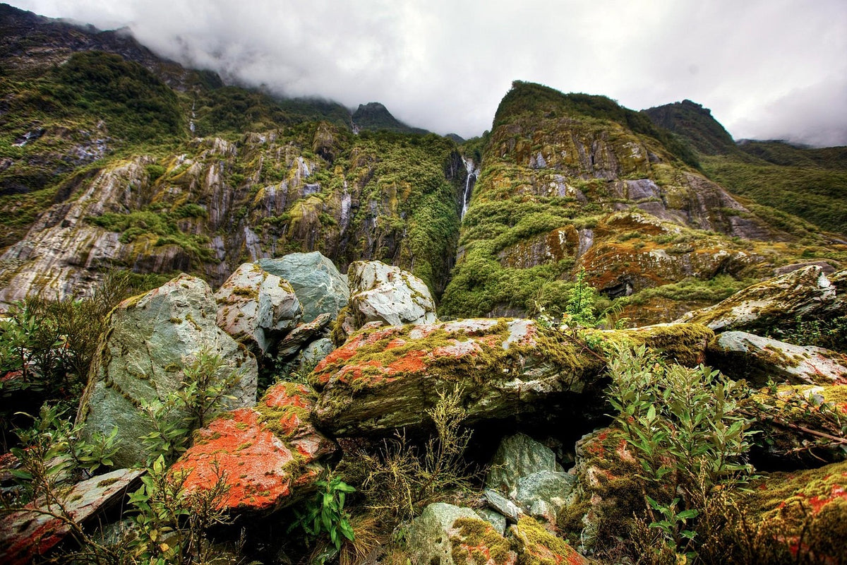 Rugged green mountains with mossy, lichen-covered boulders under clouds