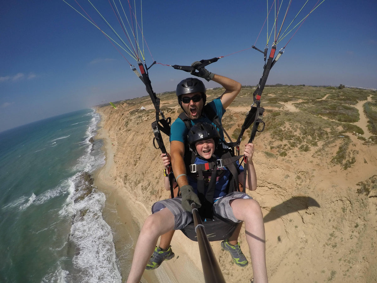 Tandem paragliding pair smiling above sandy coastal cliffs