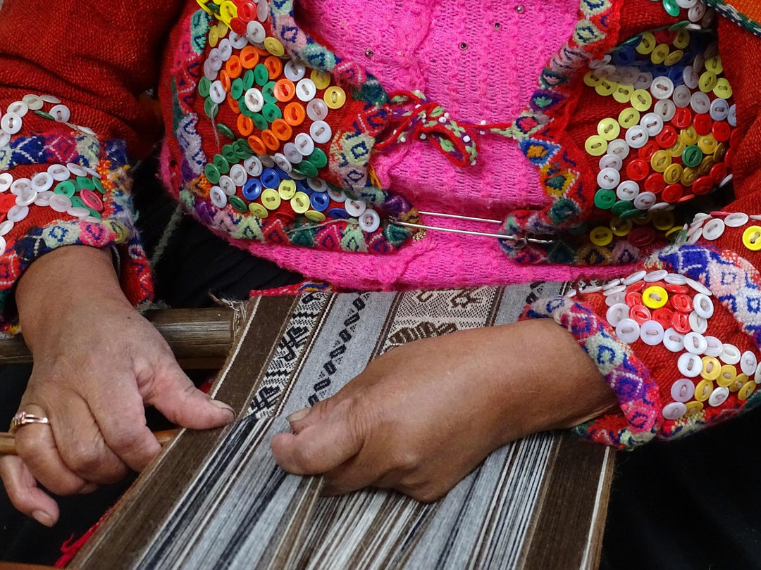 Hands weaving on a loom beside a sleeve with colourful embroidery