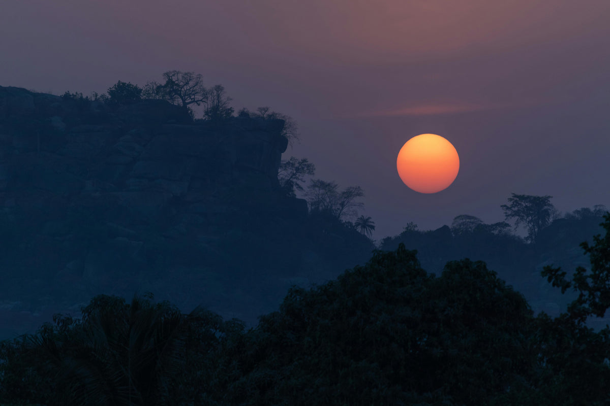Orange sun setting behind silhouetted forested hills