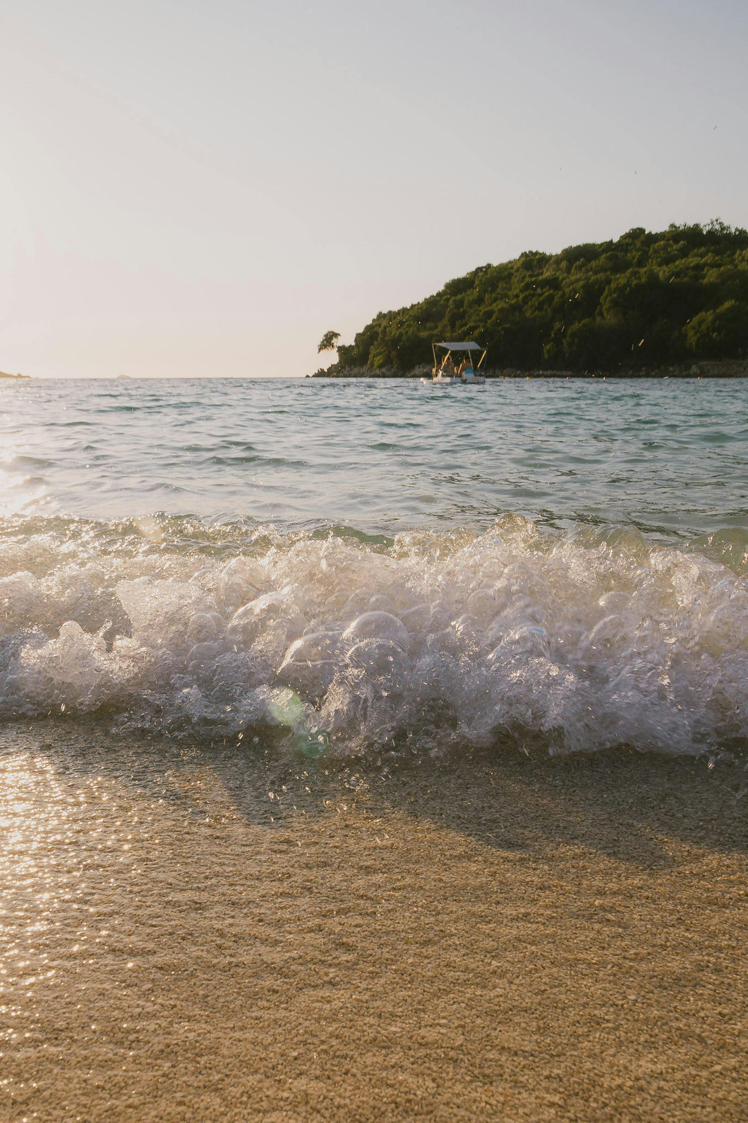 Wave breaking on a sandy beach with a green headland at sunset
