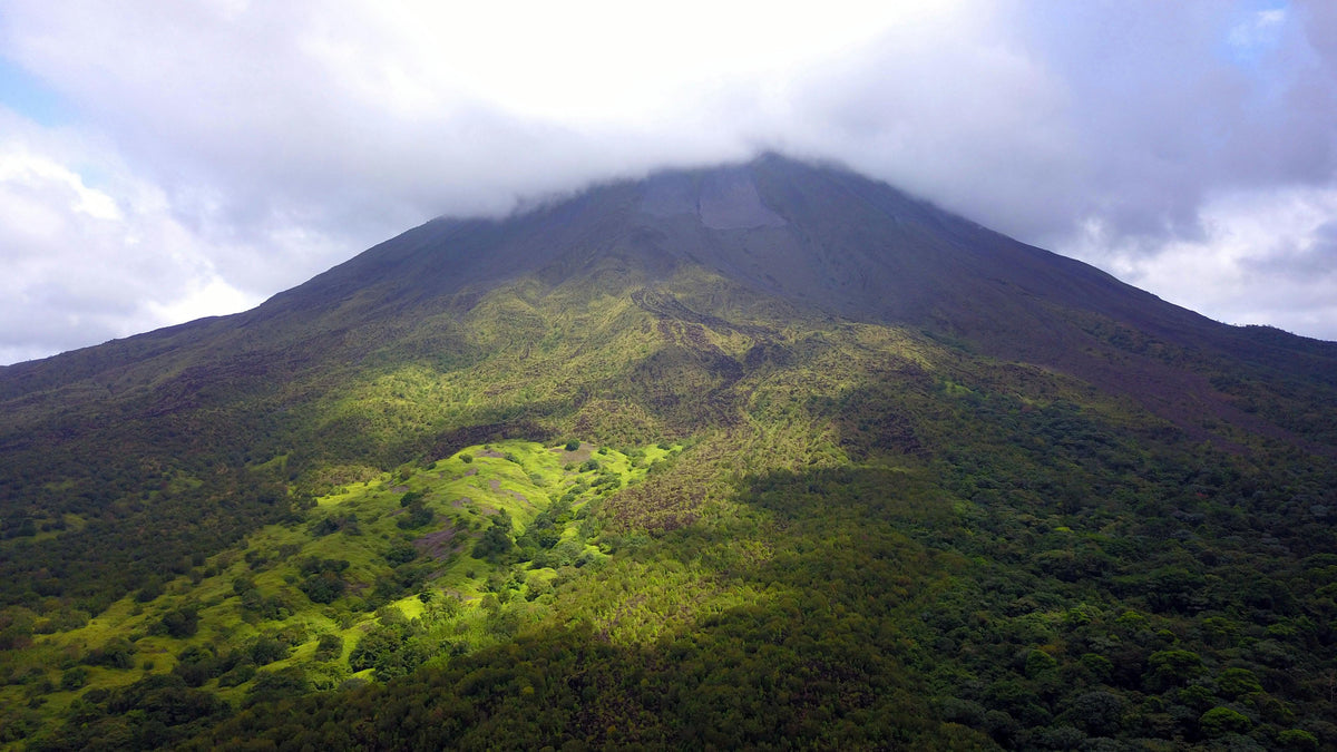 Green volcano slopes with its summit hidden in cloud