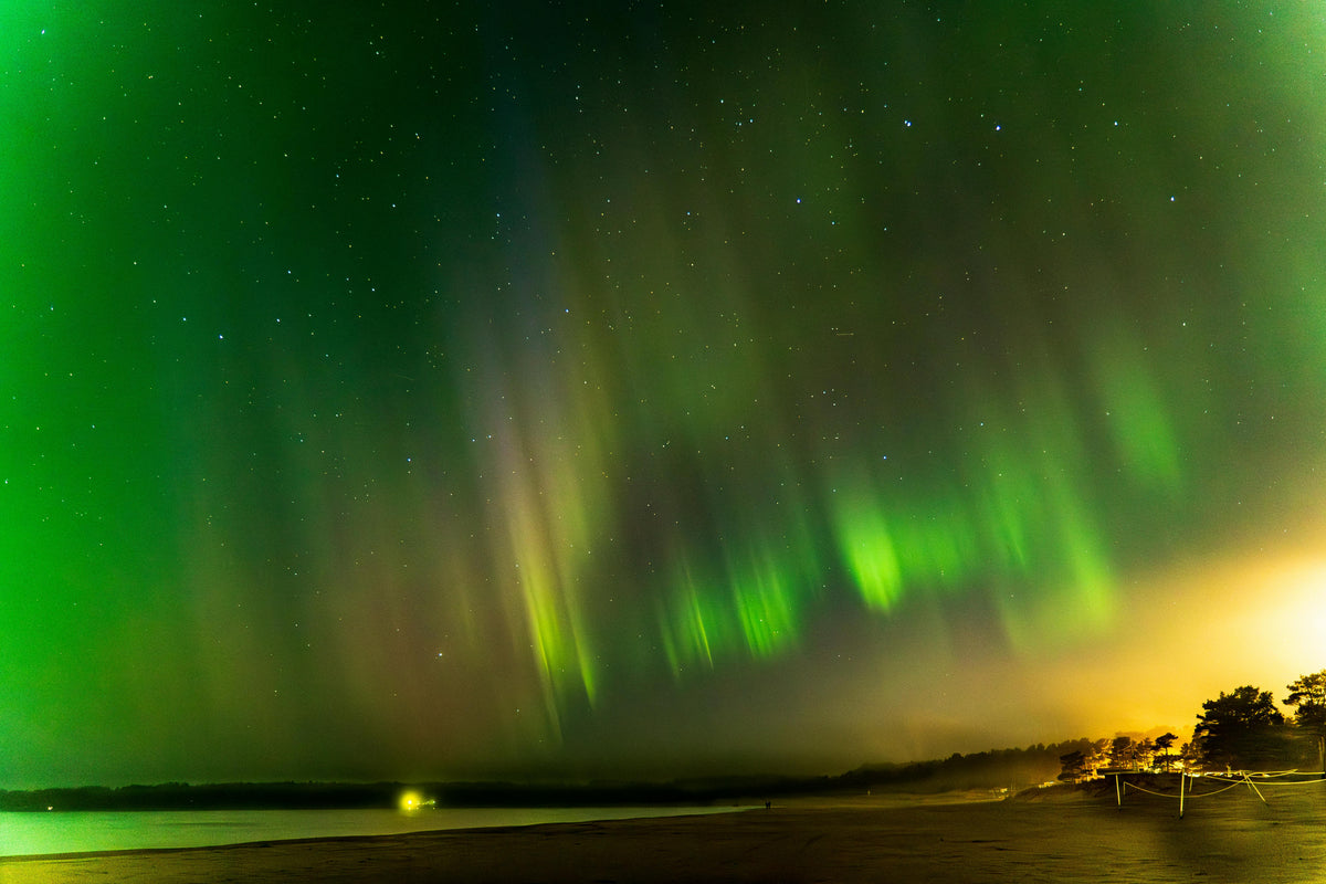 Green northern lights swirling over a dark shoreline