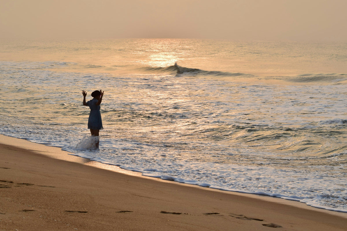 Person wading at the edge of the sea on a golden beach at sunset