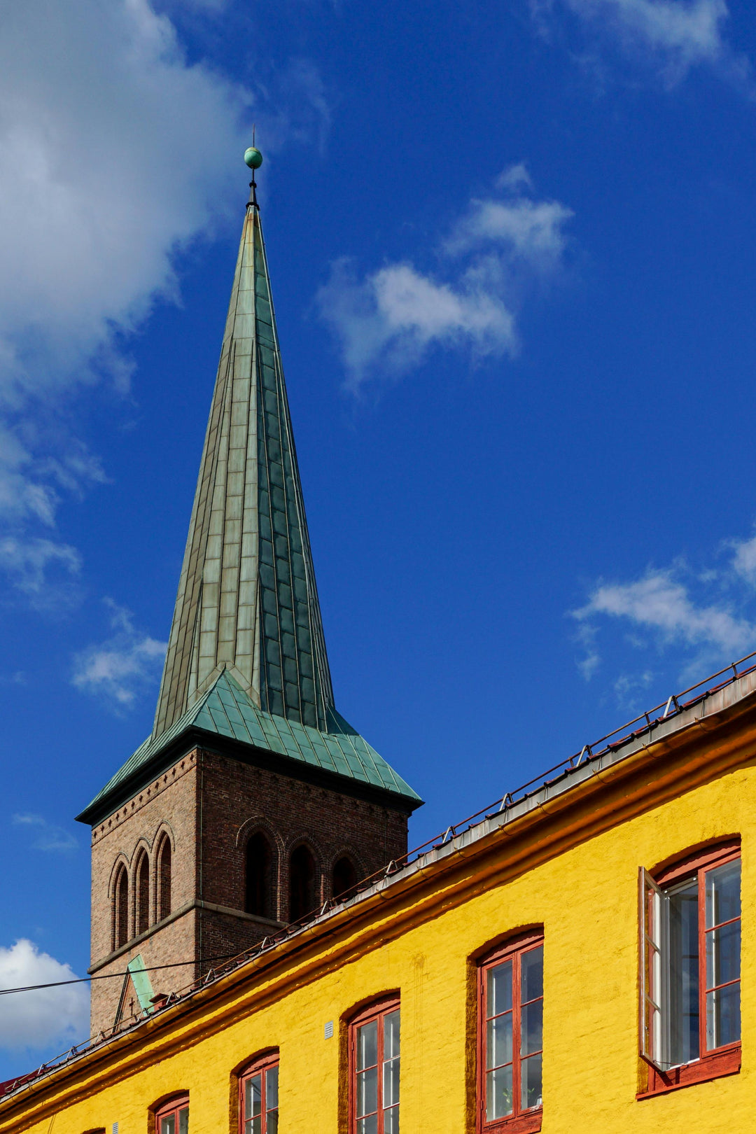 Green copper church spire above a yellow building against blue sky