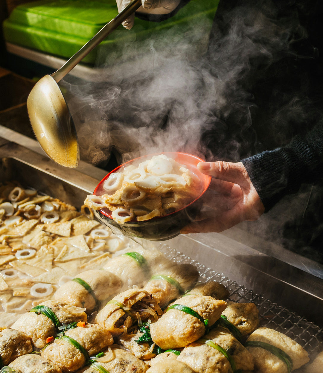 Steaming street food stall with a ladle serving fish cakes on skewers