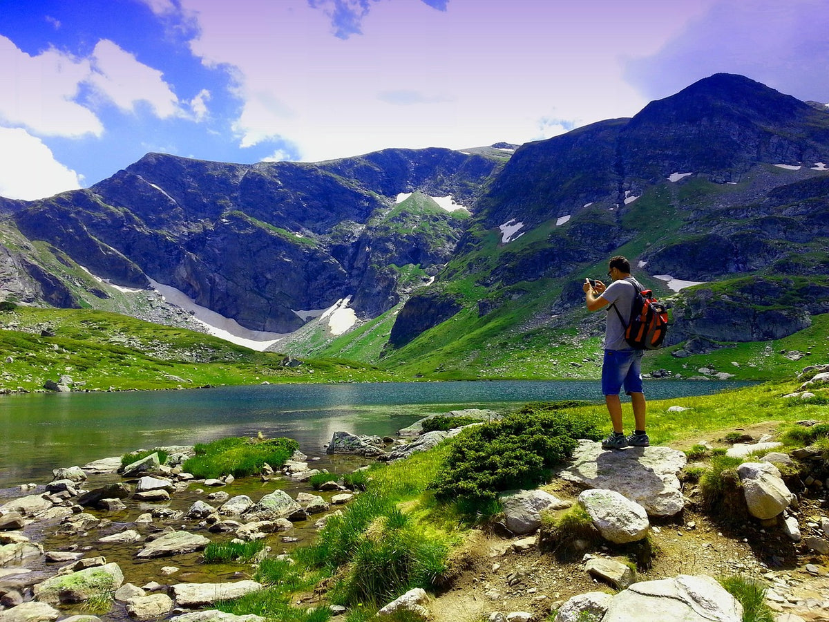 Hiker taking a photo beside a mountain lake in green valleys