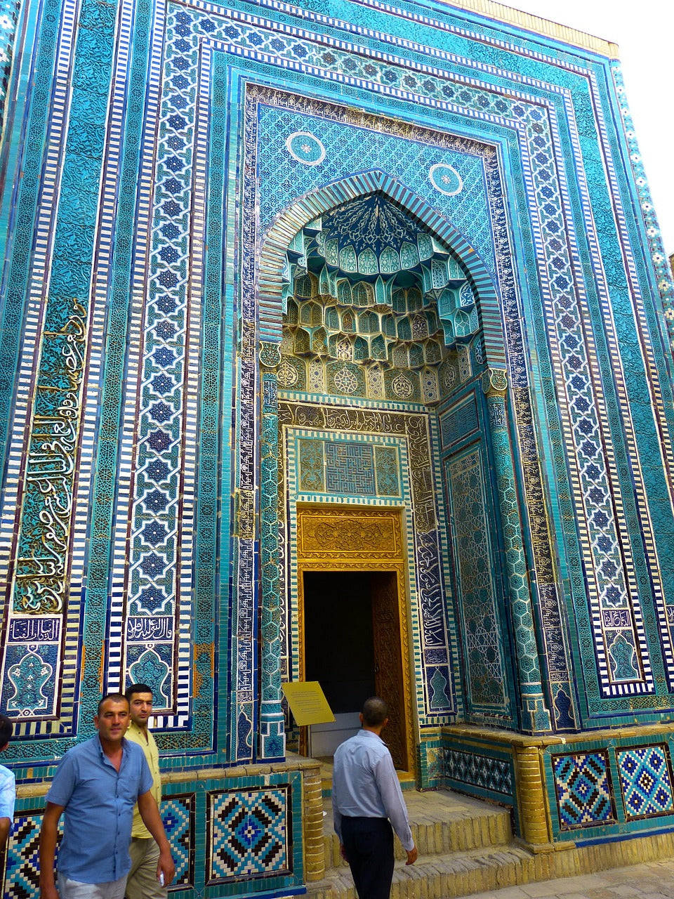 Two men outside an ornate turquoise-tiled arched doorway of a mausoleum
