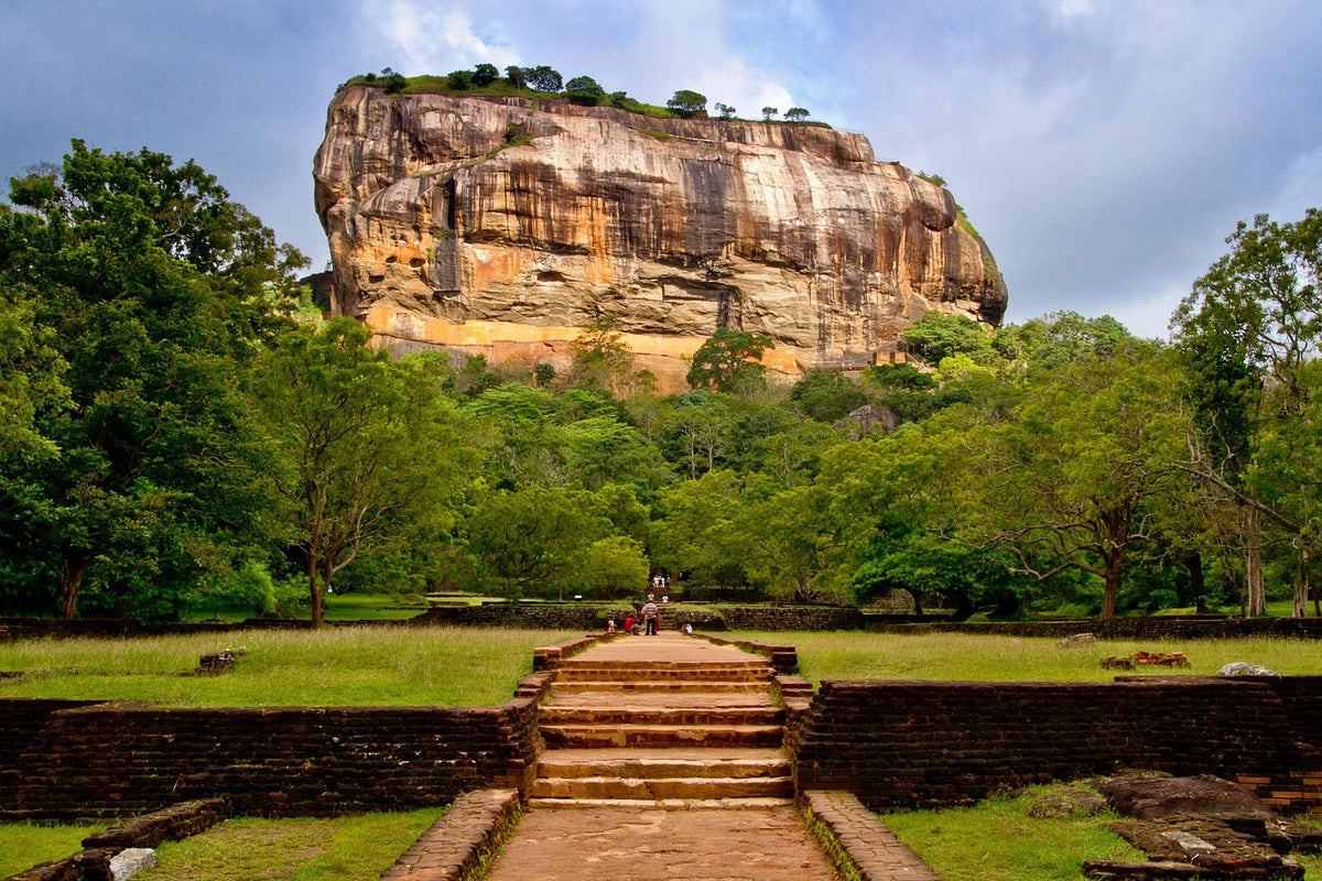 Massive flat-topped rock rising above green gardens and a stone stairway