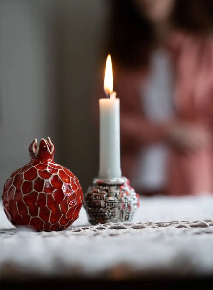 Lit white candle beside a red pomegranate ornament on a table