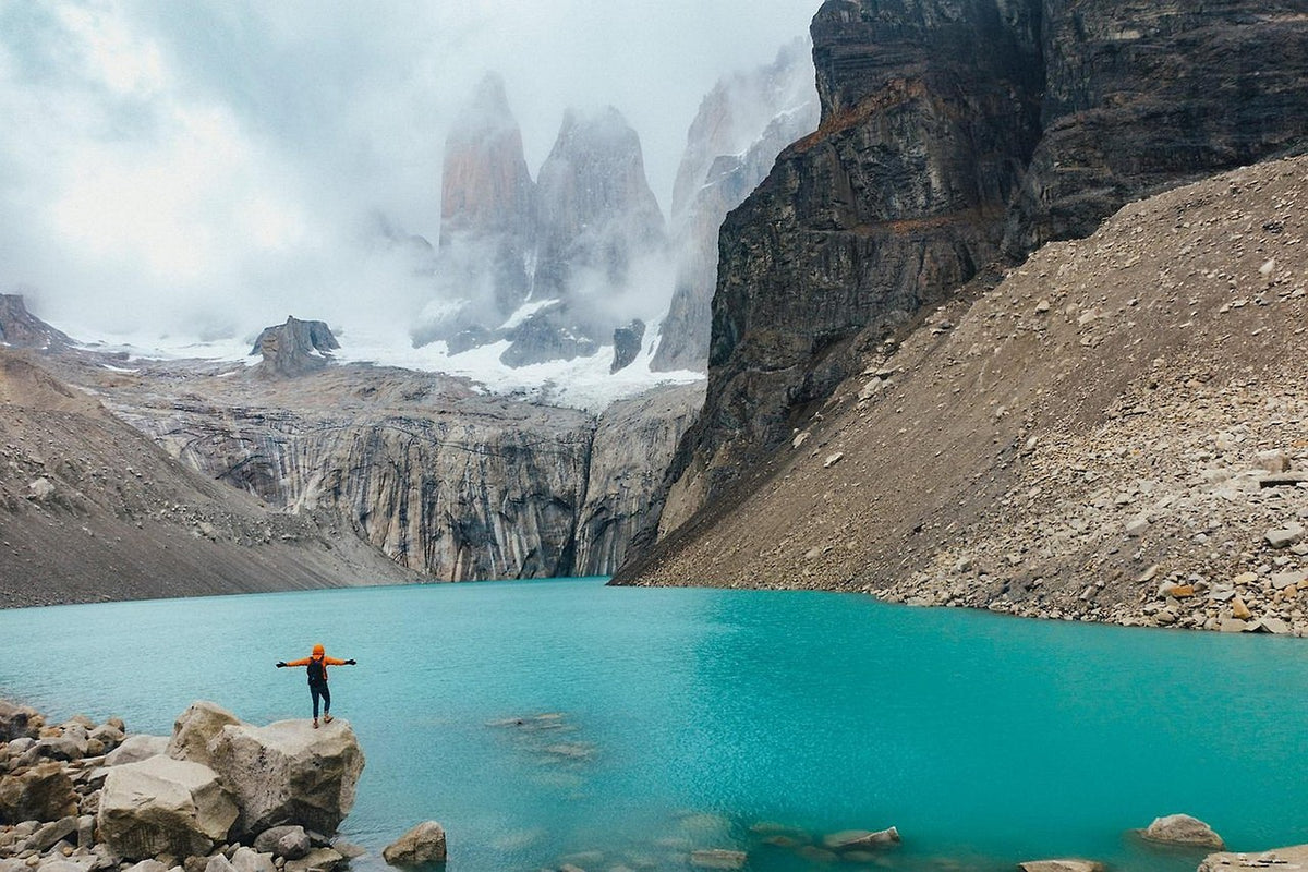 Hiker by a turquoise glacial lake below jagged granite towers