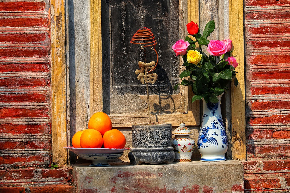 Street shrine with oranges, roses in a blue vase and incense on red brick